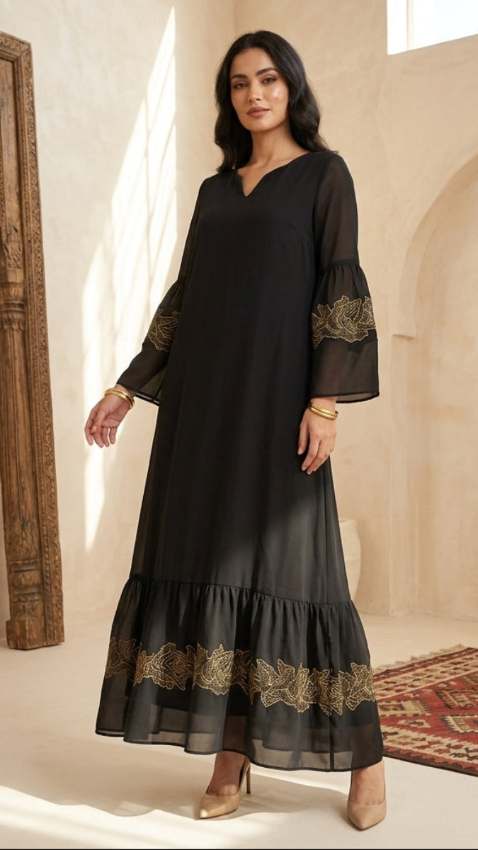 Woman wearing a black dress with gold embroidery in a decorative room.
