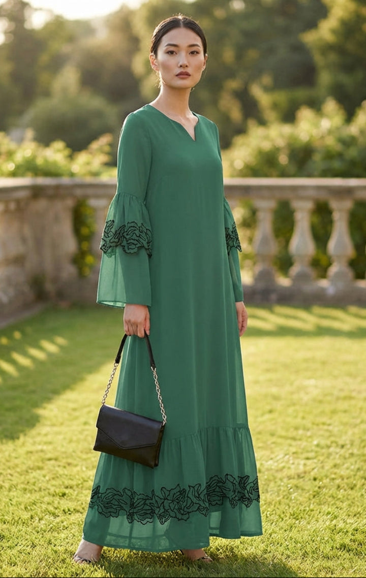 Woman in a green dress standing on grass with a stone wall and trees in the background