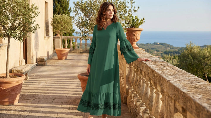 Woman in a green dress standing on a stone balcony with a scenic view.