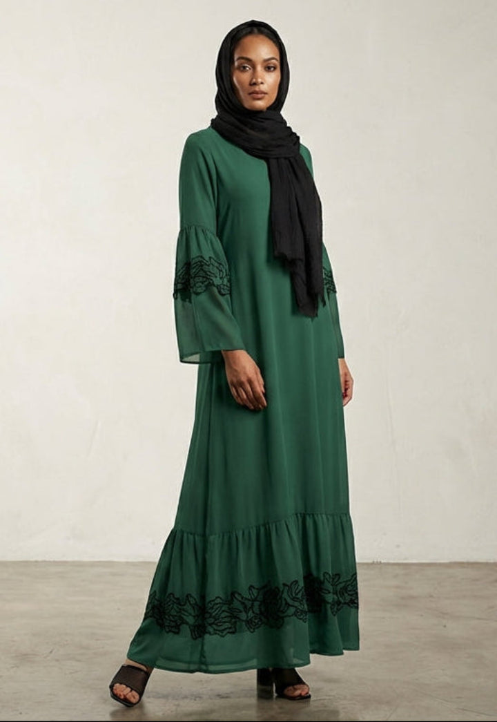 Woman wearing a green dress with black hijab against a plain background