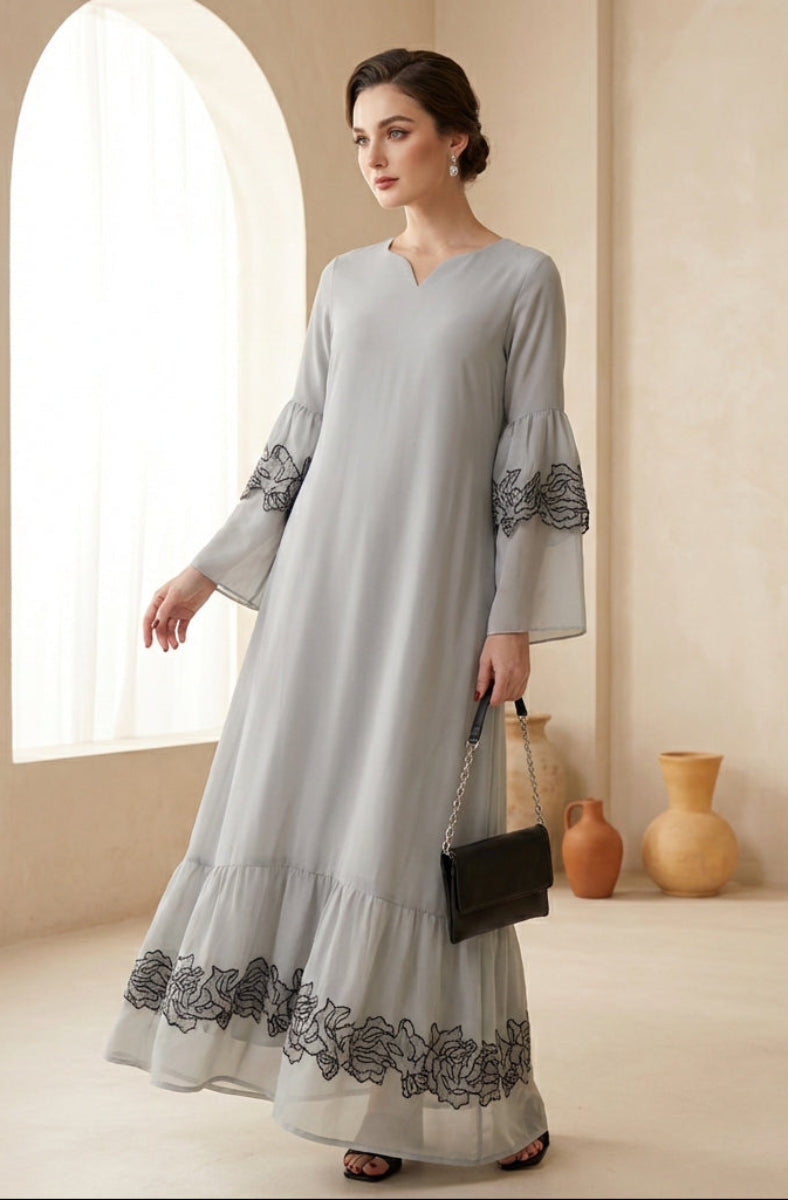Woman wearing a light gray dress with black embroidery in a bright room.