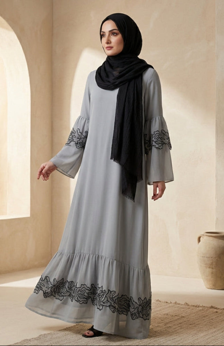 Woman wearing a gray dress with black embroidery in a warm-toned room.