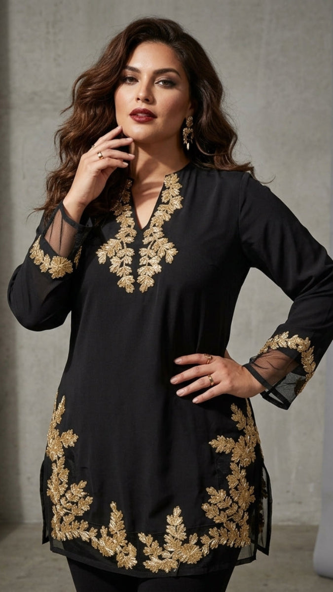 A woman models a black long kurta with ornate gold floral embroidery around the neckline, cuffs, and hem, set against a neutral gray studio backdrop.