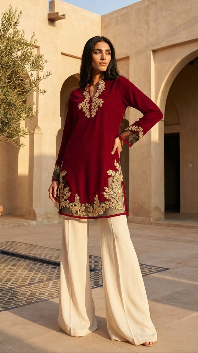 Woman in a red embroidered outfit standing in a sunlit courtyard with architectural elements.