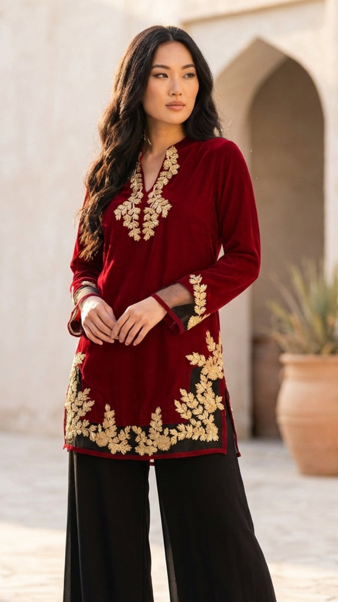 Woman wearing a red embroidered top with gold details in an outdoor setting.