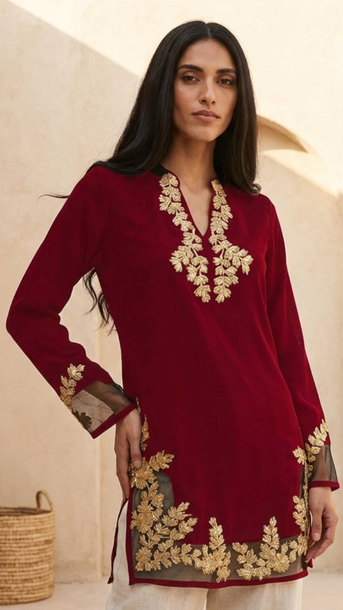 Woman wearing a red embroidered dress in a neutral setting with plants.