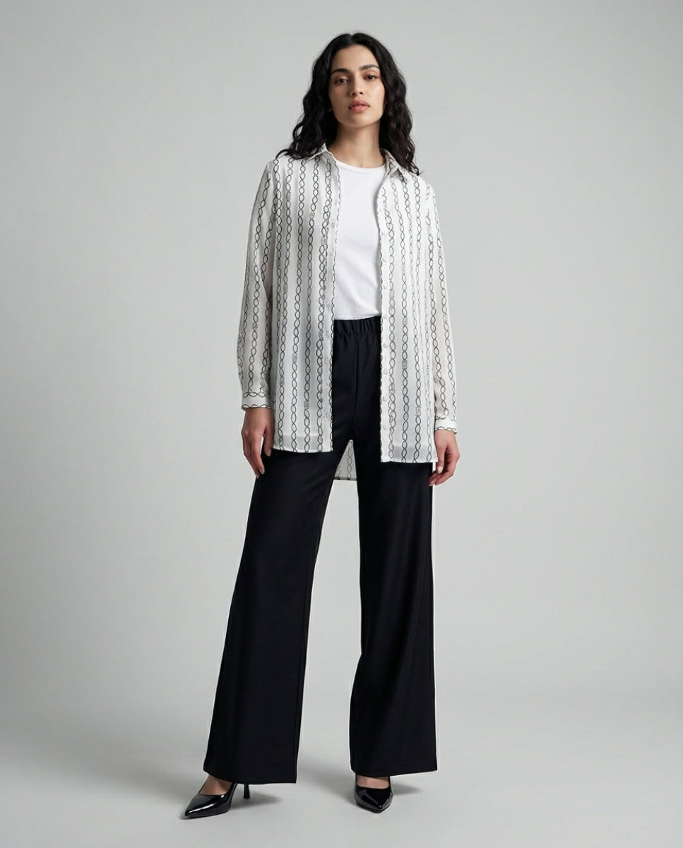Woman wearing a white blouse with black patterns and black pants on a gray background