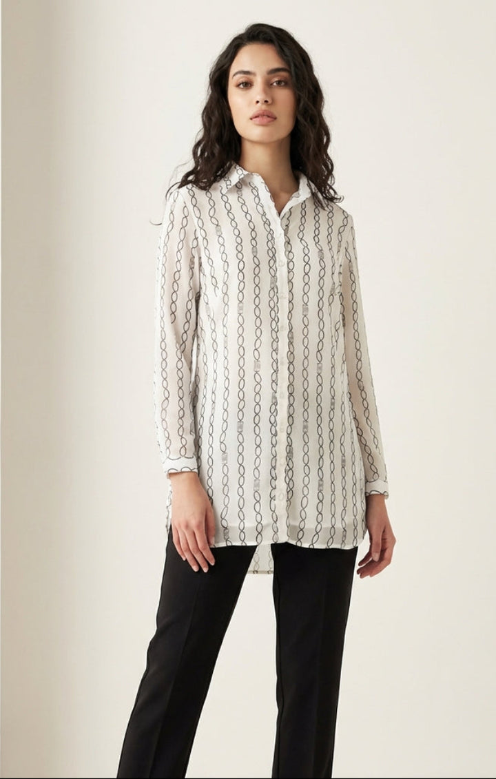 Woman wearing a white blouse with black patterns and black pants on a light beige background