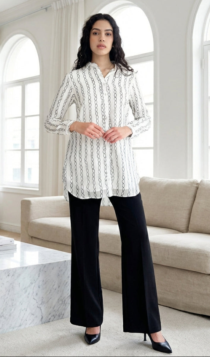 Woman in a white patterned shirt and black pants standing in a modern living room.