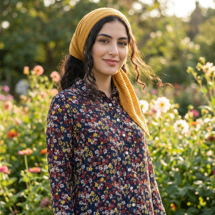 Woman wearing a yellow knitted headscarf in a garden with flowers
