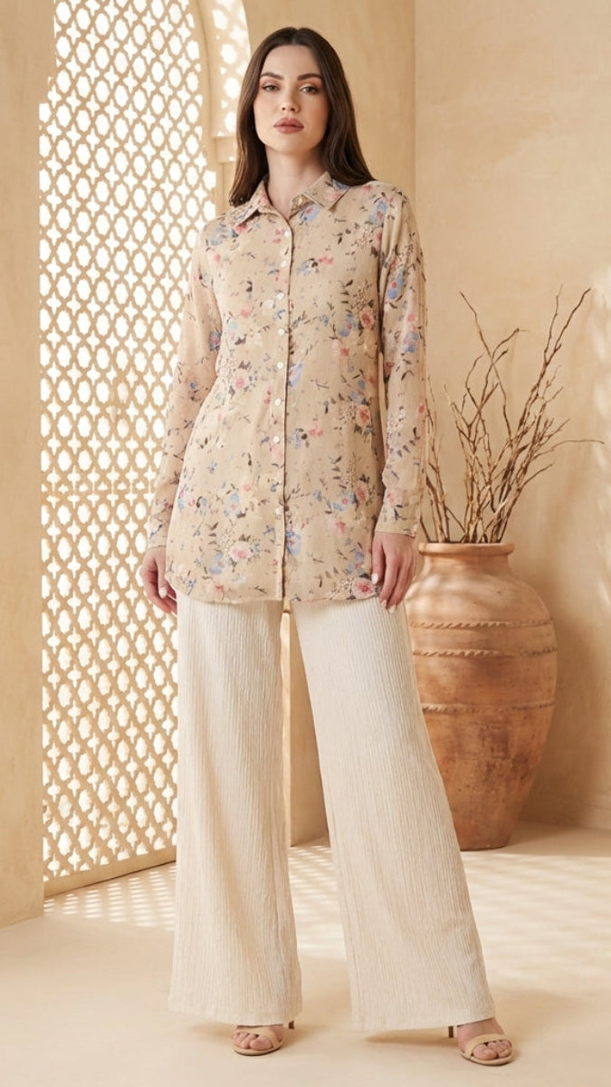 Woman wearing a floral blouse and white pants standing in a decorative room with a vase and lattice wall.