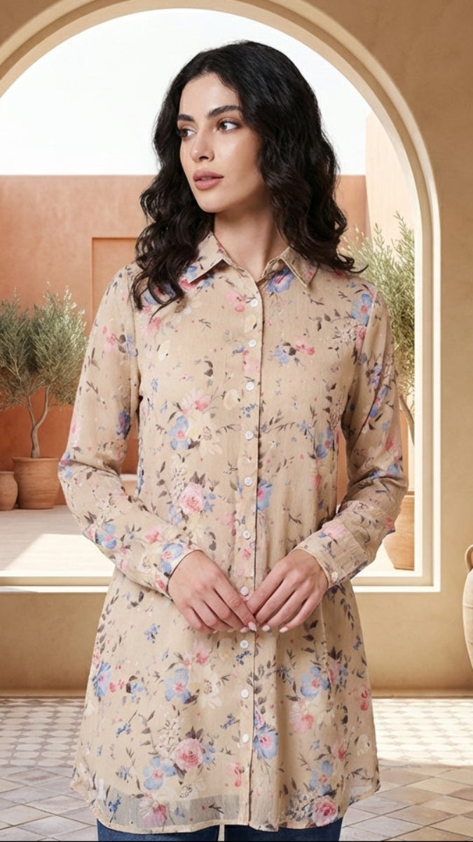 Woman wearing a floral beige shirt standing in a sunlit room with archway and decorative vases.