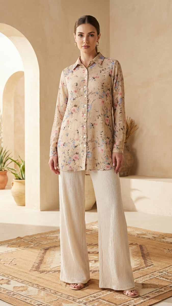 Woman in a floral blouse and beige pants standing in a sunlit room with arches and plants.