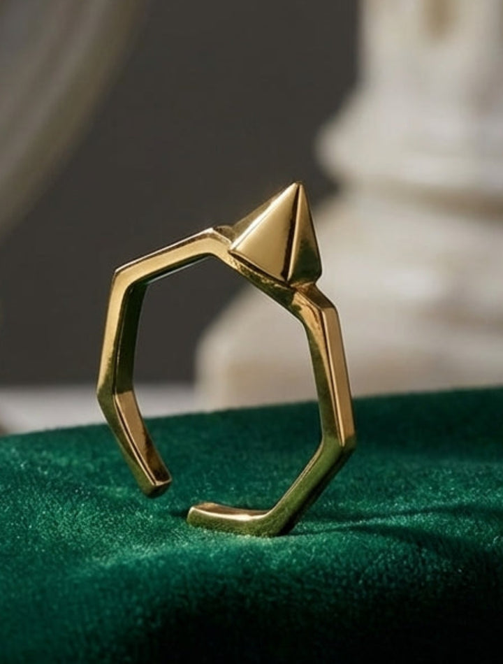 Gold geometric ring on a green surface with classical architecture in the background