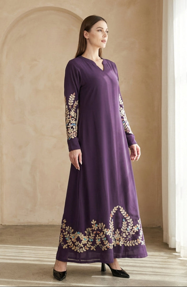 Woman wearing a long purple dress with floral patterns in a neutral setting