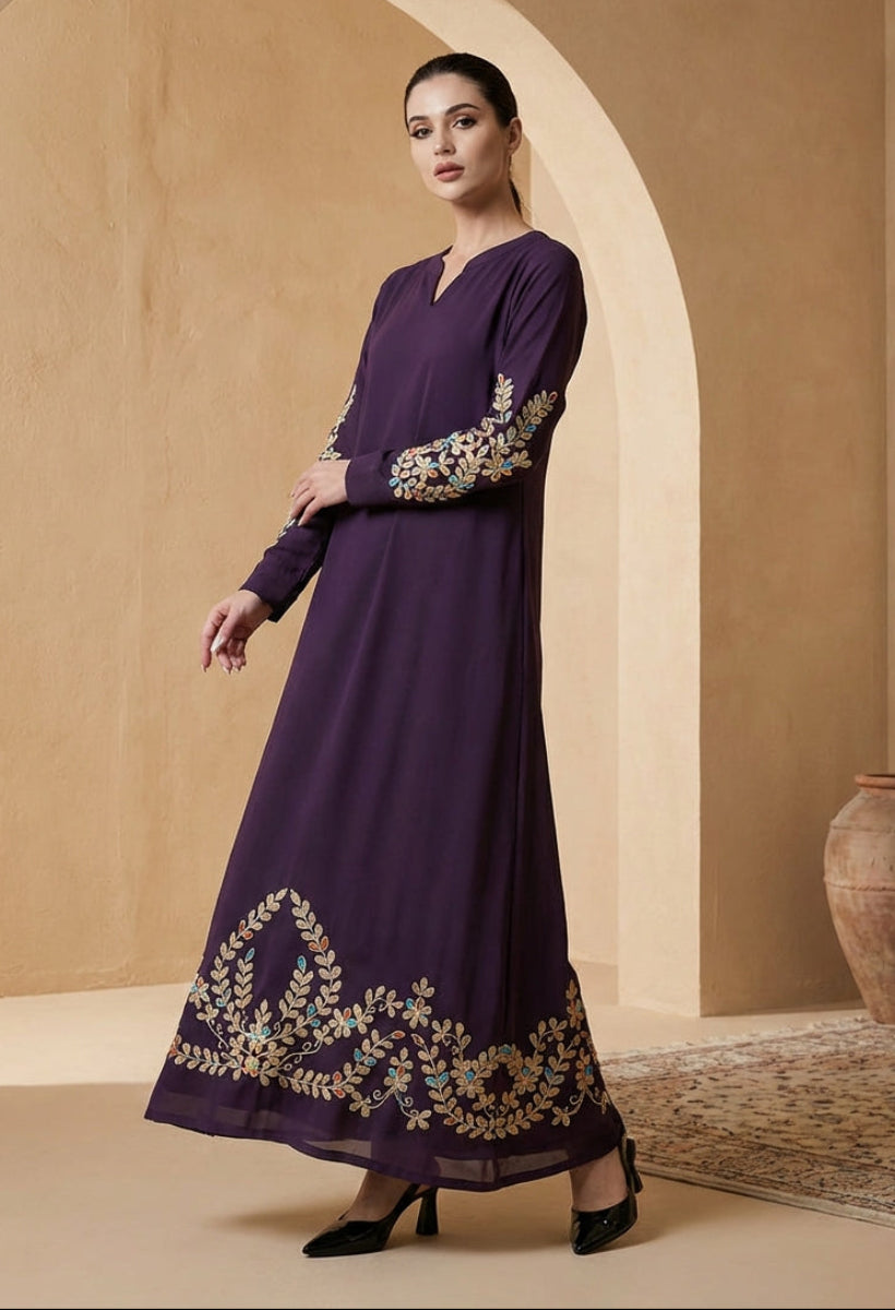 Woman wearing a long purple dress with gold embroidery in a warm-toned interior setting.