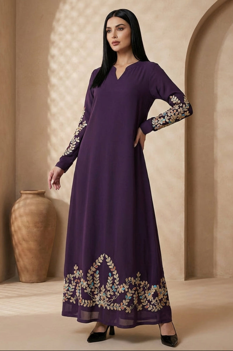 Woman wearing a long purple dress with floral embroidery in a warm-toned room.