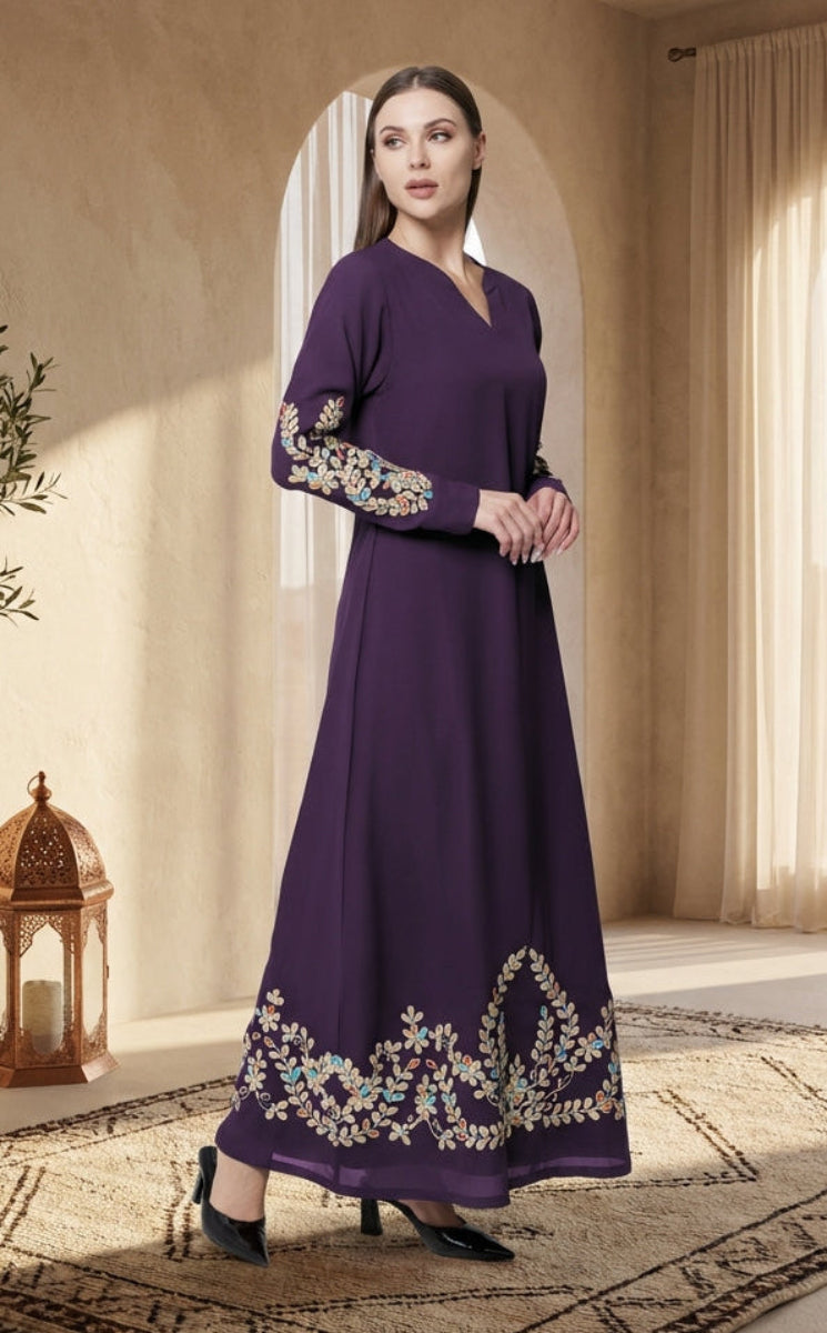 Woman in a long purple dress with floral embroidery standing in a sunlit room with decor elements.