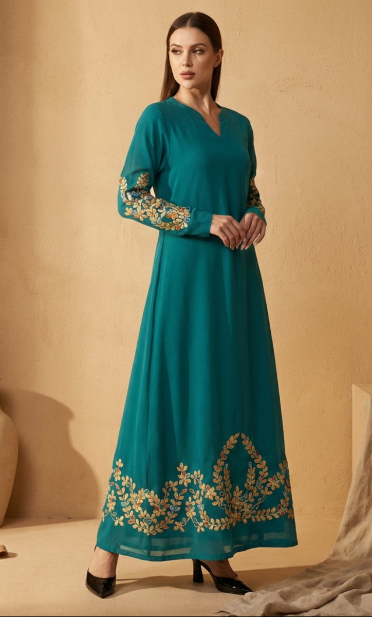 Woman wearing a teal dress with gold embroidery against a beige background