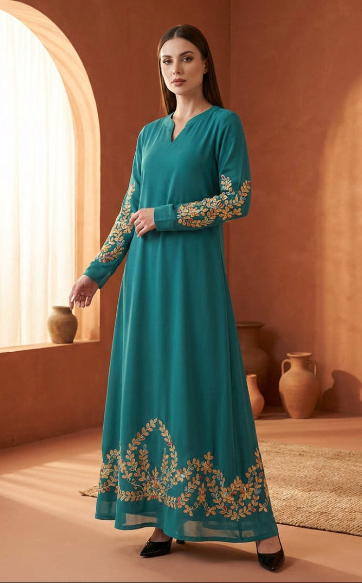 Woman wearing a teal dress with gold embroidery in a warm-toned room.