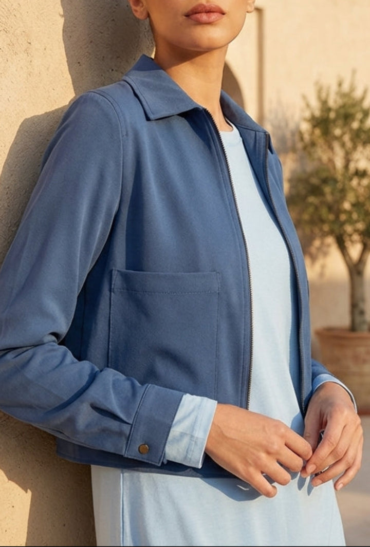 Woman in a blue jacket standing against a beige wall with a building in the background