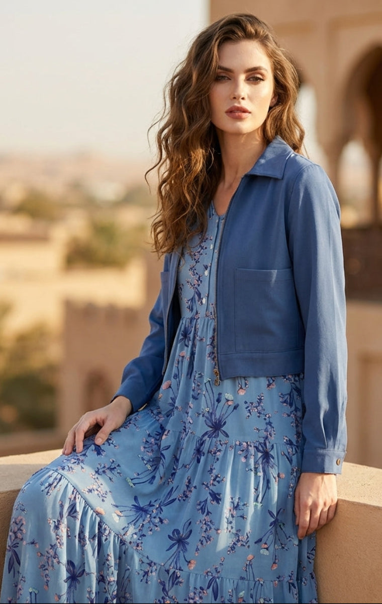 Woman in a blue floral dress and jacket standing on a balcony with a scenic background