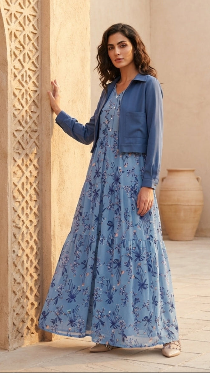 Woman in a blue floral dress standing in a sunlit outdoor setting with architectural elements.