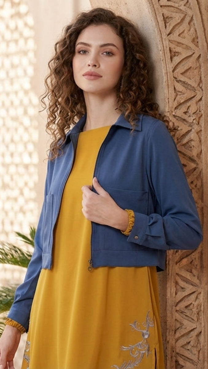 Woman in a yellow dress and blue jacket standing in a decorative outdoor setting.
