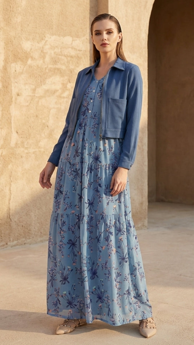 Woman wearing a blue floral dress and jacket standing in front of a beige wall with an arch.