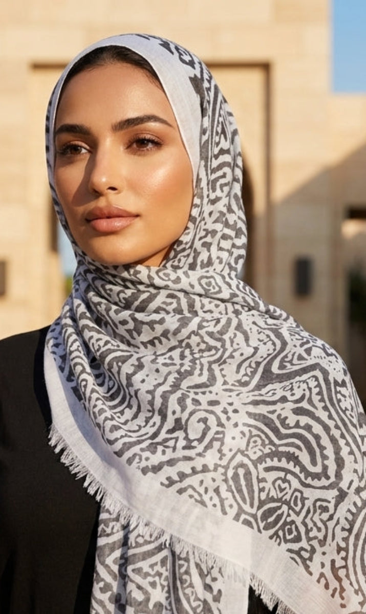 Woman wearing a patterned hijab in an outdoor setting with architectural elements.
