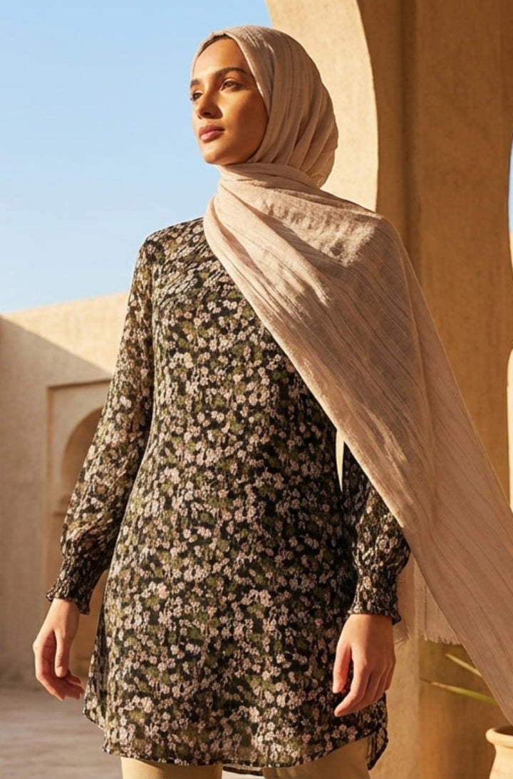 Woman in a hijab standing in a sunlit courtyard with architectural elements and plants.