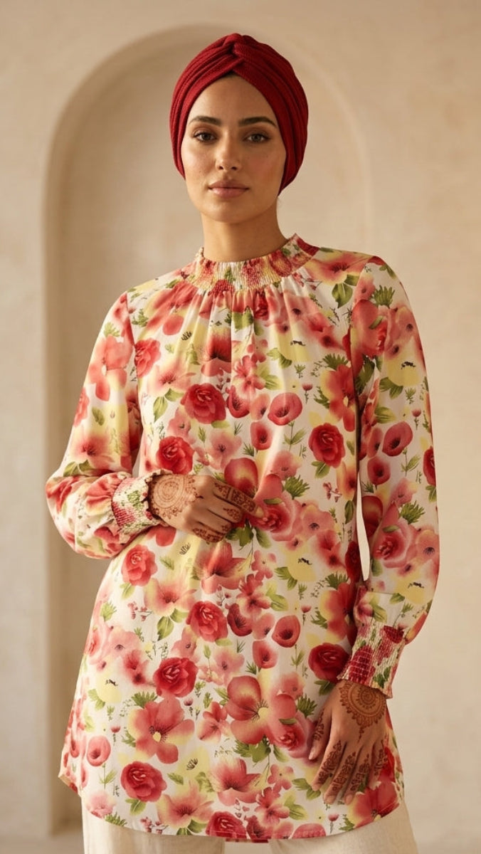 Woman wearing a floral blouse and red headscarf in an arched room.