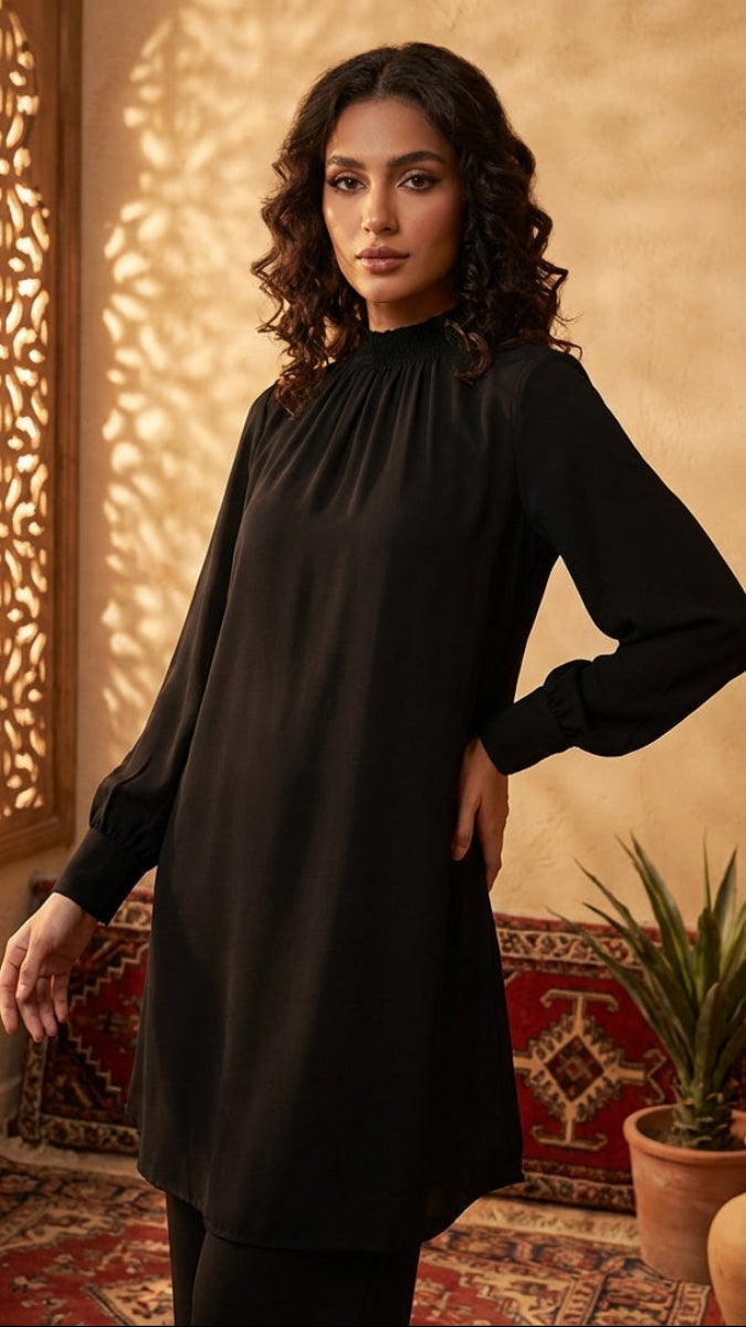 Woman in a black dress standing in a room with decorative wall patterns and plants.