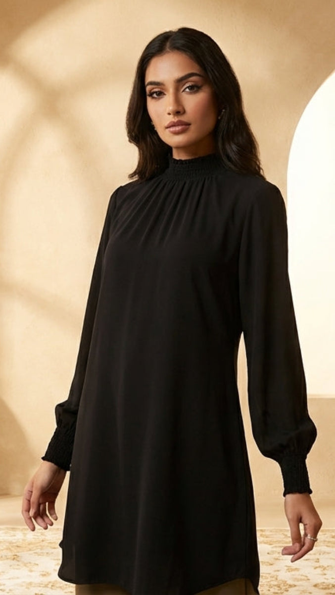 Woman in a black dress standing in a sunlit room with architectural elements and decorative items.