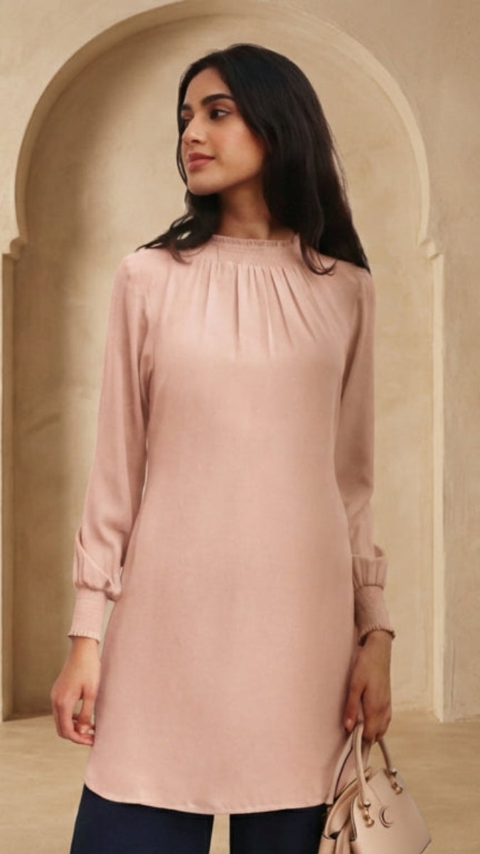 Woman wearing a light pink dress standing in a room with beige walls and wooden floor.
