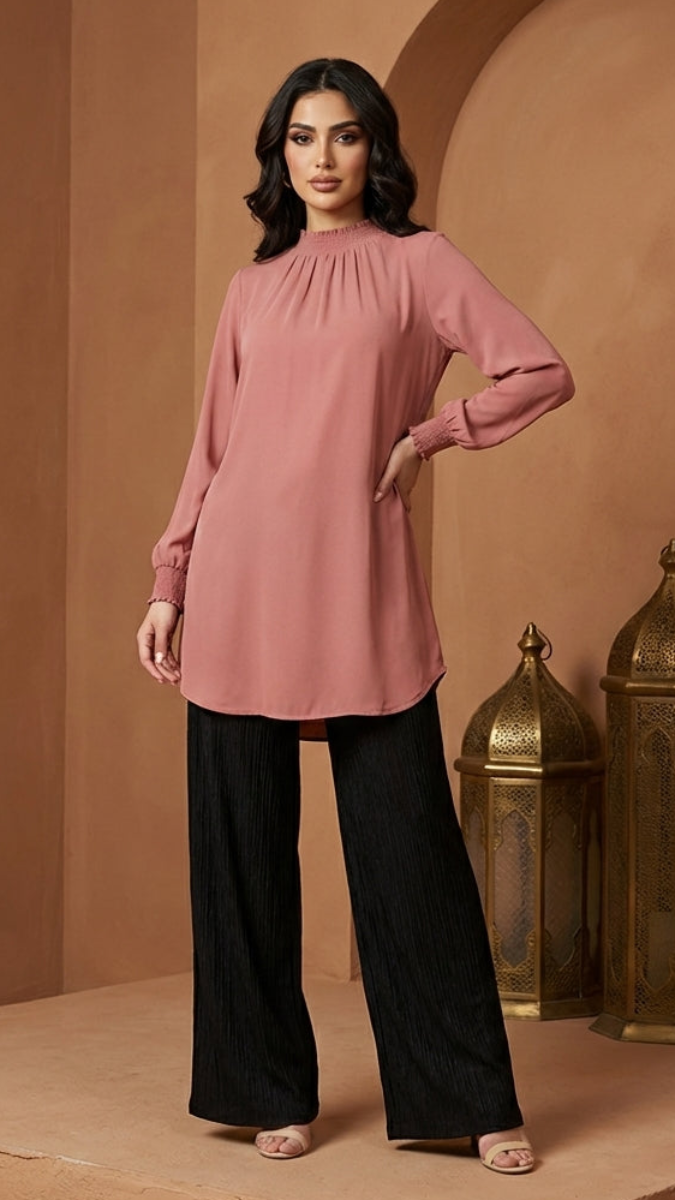 Woman wearing a pink blouse and black pants in a warm-toned interior setting with lanterns.