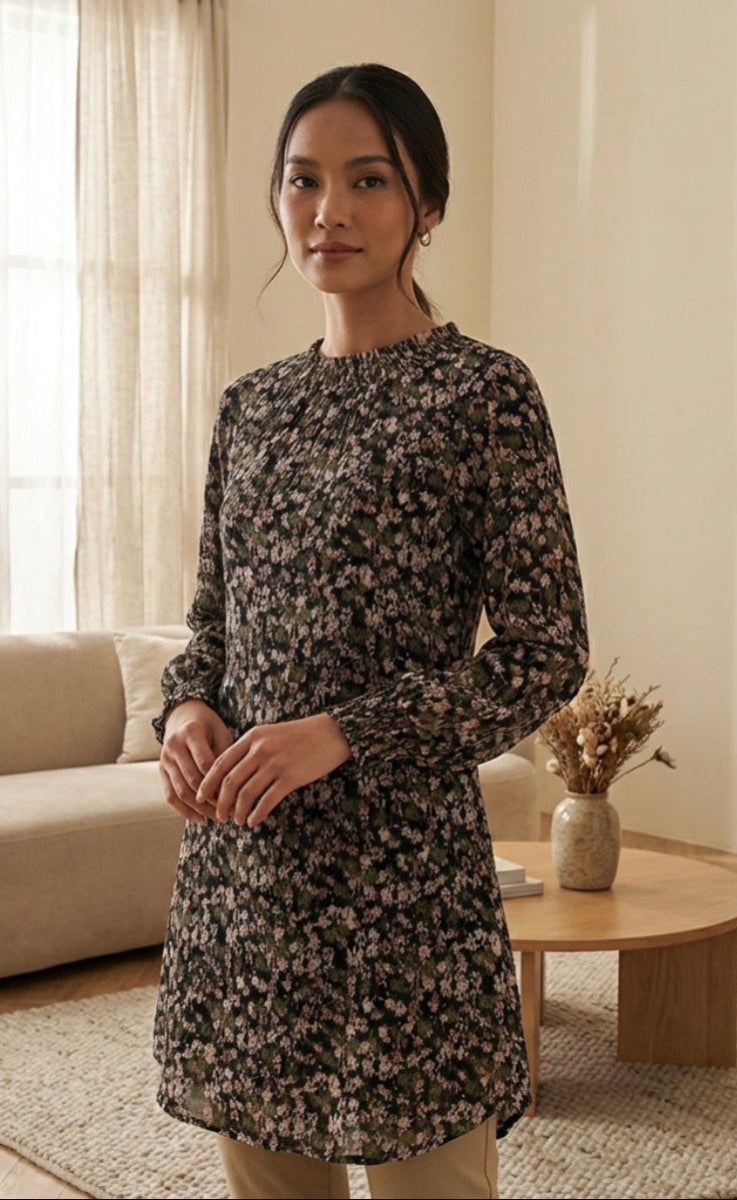 Woman in a floral dress standing in a living room with a couch and coffee table.