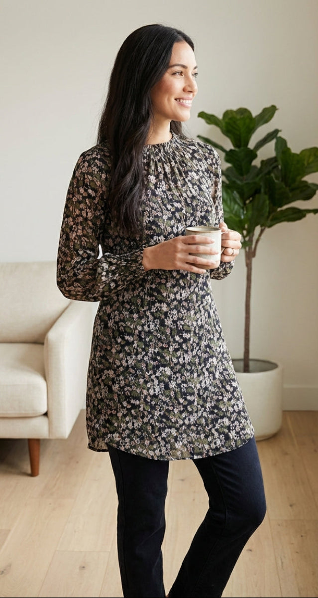 Woman in a floral dress holding a mug in a room with a couch and plant.