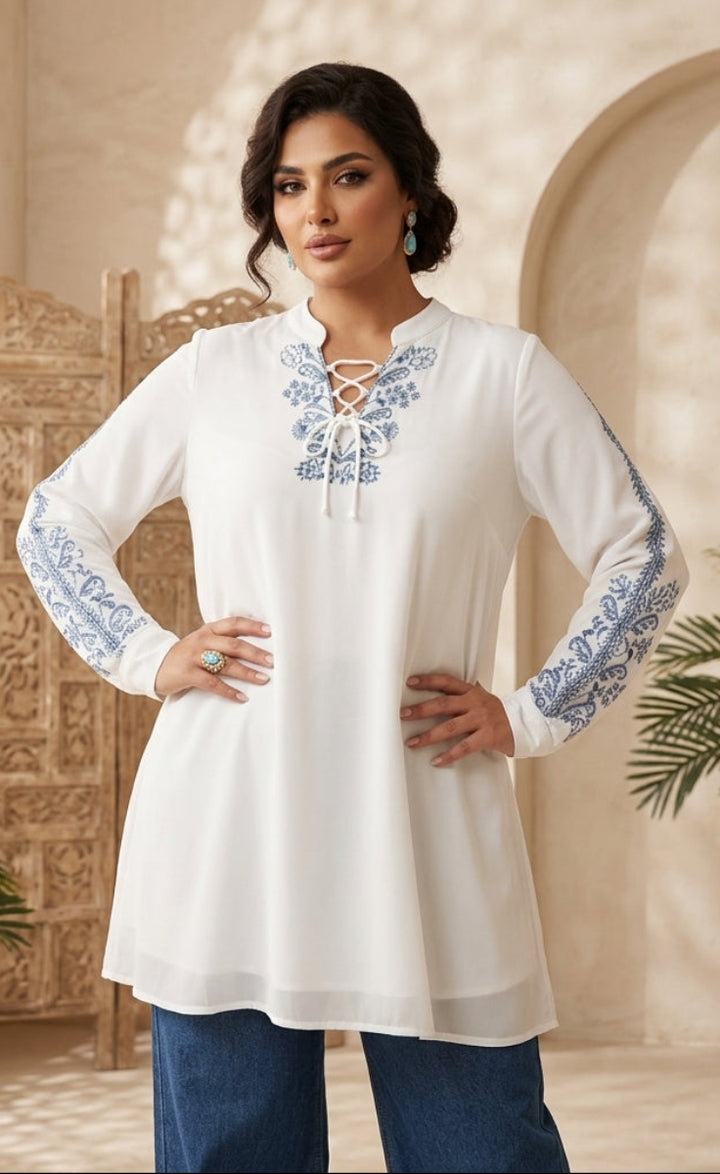 Woman wearing a white embroidered top in an ornate room with plants.