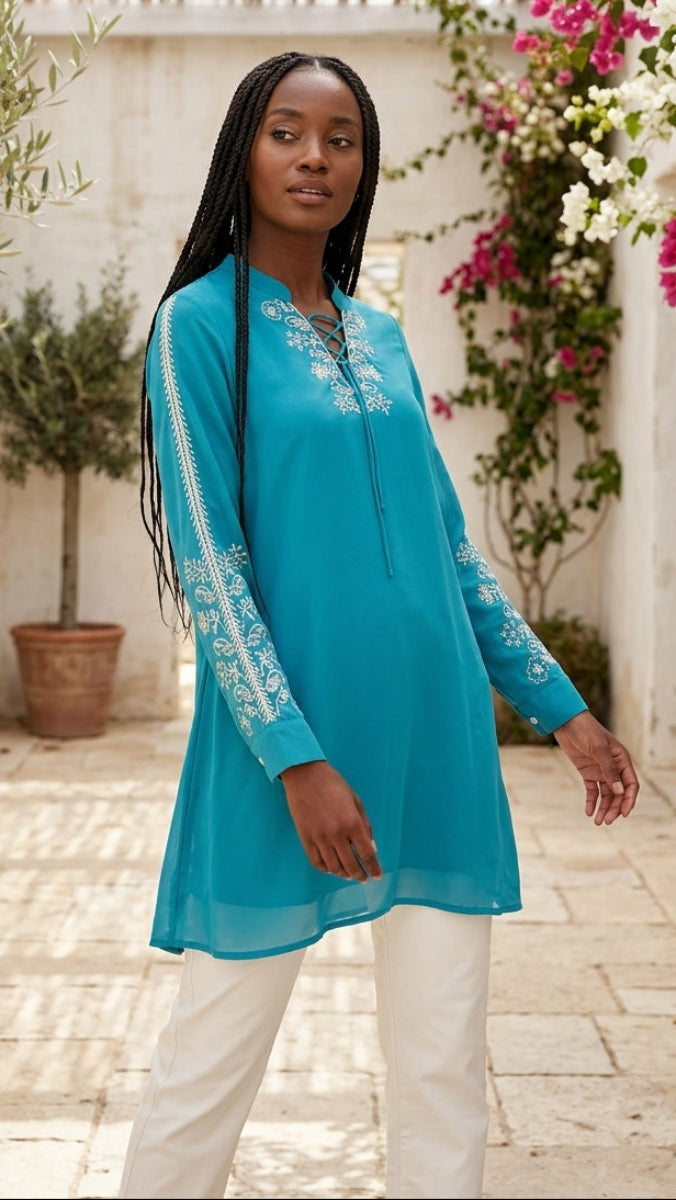 Woman wearing a blue embroidered dress standing in a decorative outdoor setting with flowers and plants.