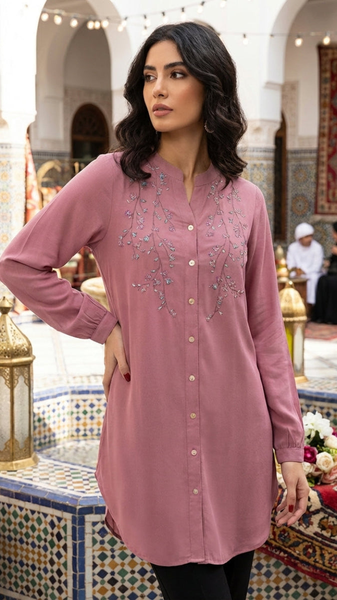 Woman wearing a pink embroidered dress in an ornate indoor setting.