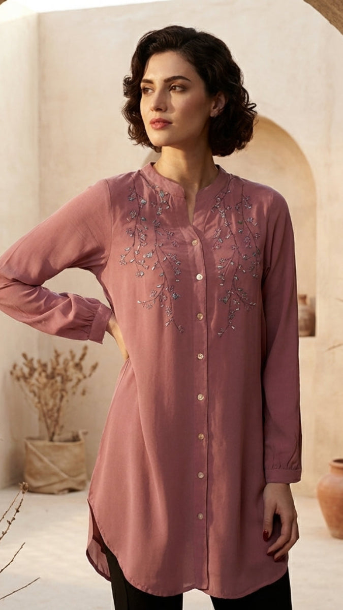 Woman wearing a pink embroidered dress in a warm-toned interior setting