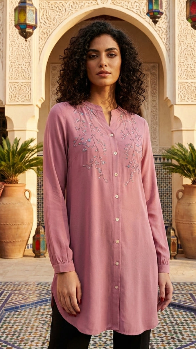 Woman wearing a pink embroidered shirt in a decorative courtyard.
