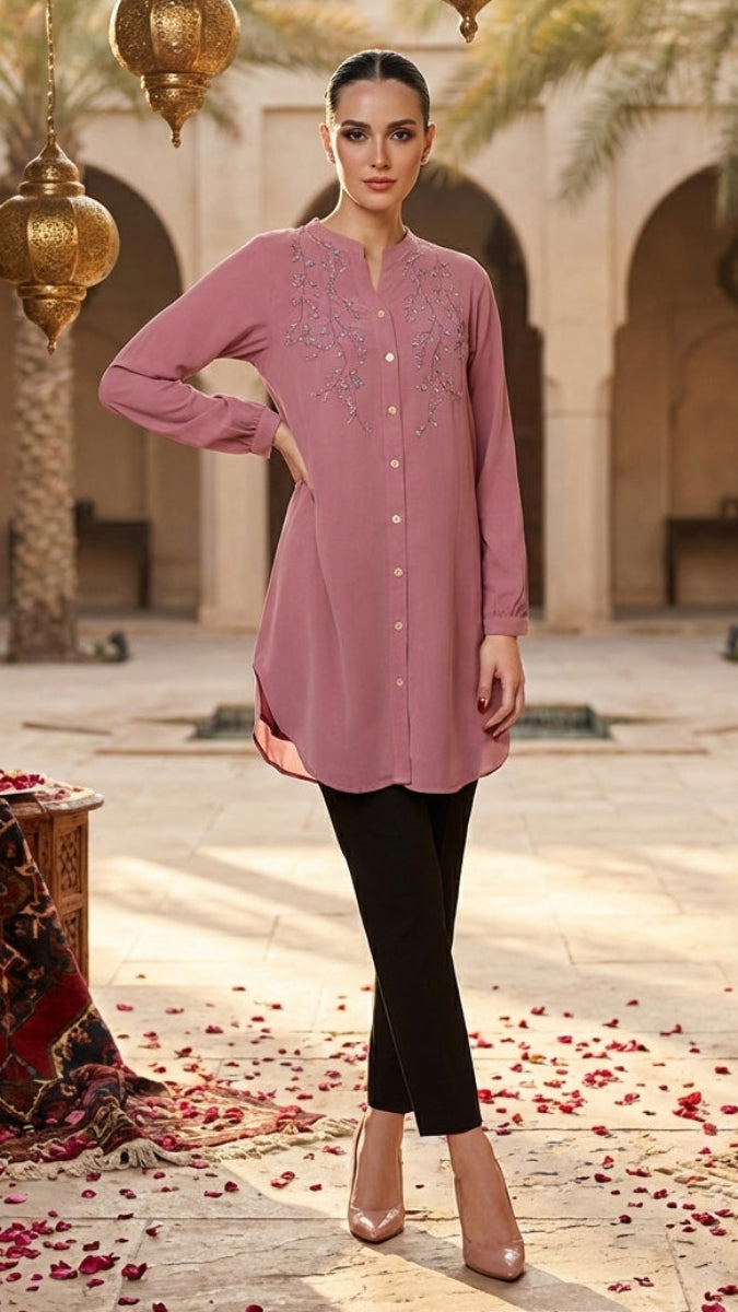 Woman in a pink embroidered shirt and black pants standing in an ornate courtyard with hanging lanterns.