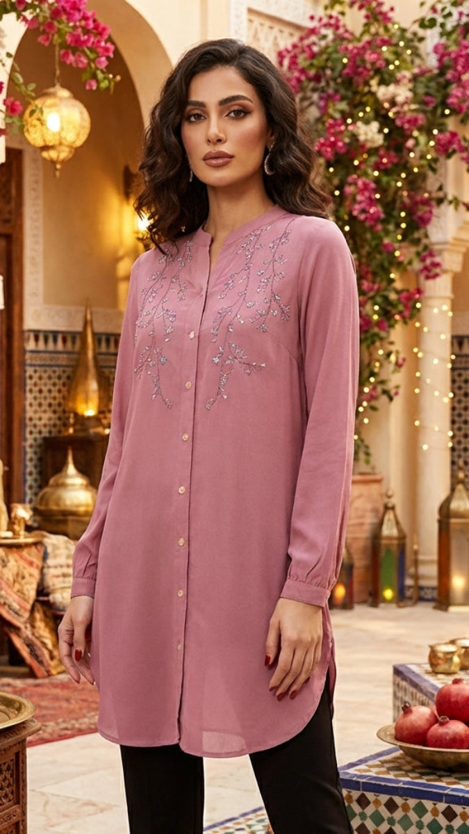 Woman in a pink embroidered dress standing in a decorative interior setting with flowers and lanterns.