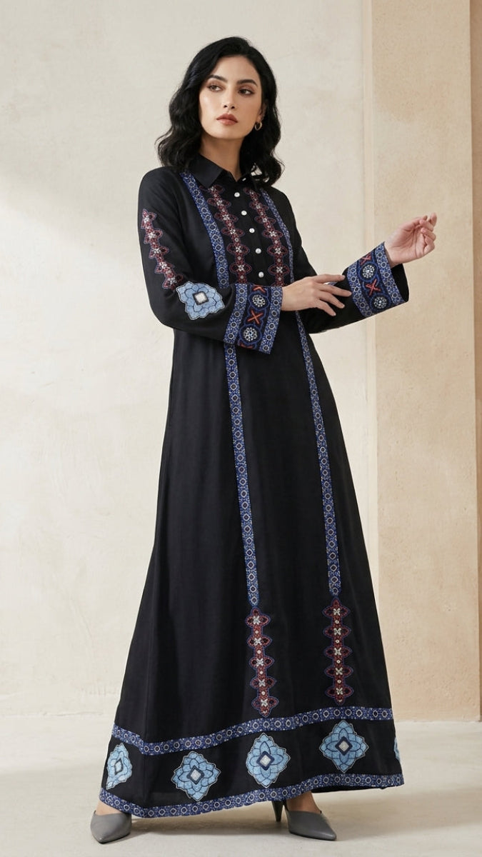 A woman modeling a long black embroidered kurta with blue, red, and white geometric patterns along the front, sleeves, cuffs, and hem, set against a neutral beige background.