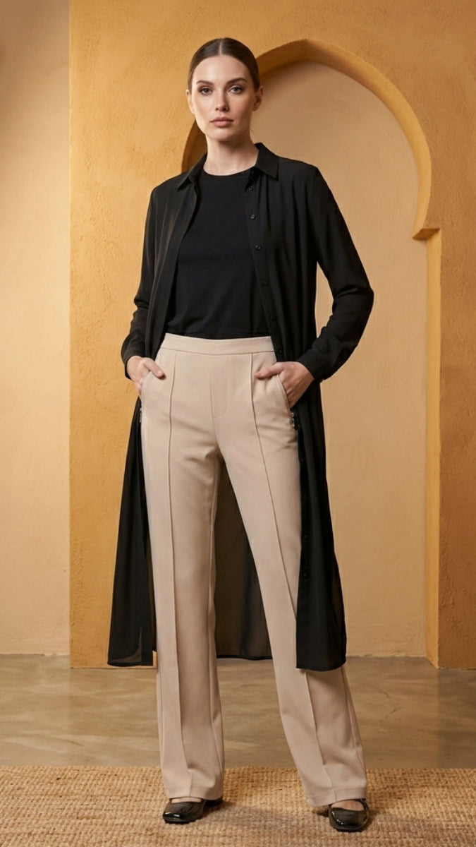 Woman in black shirt and beige pants standing in a warm-toned room with an archway.