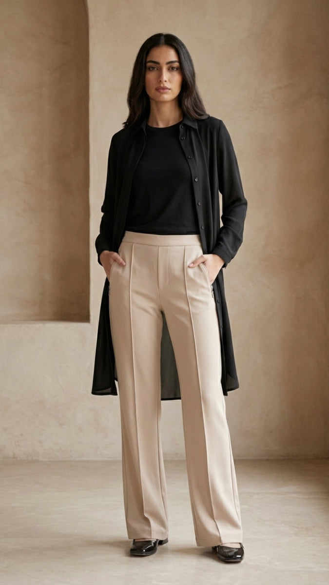 Woman wearing a black shirt and beige pants in a minimalistic room with a neutral color palette.