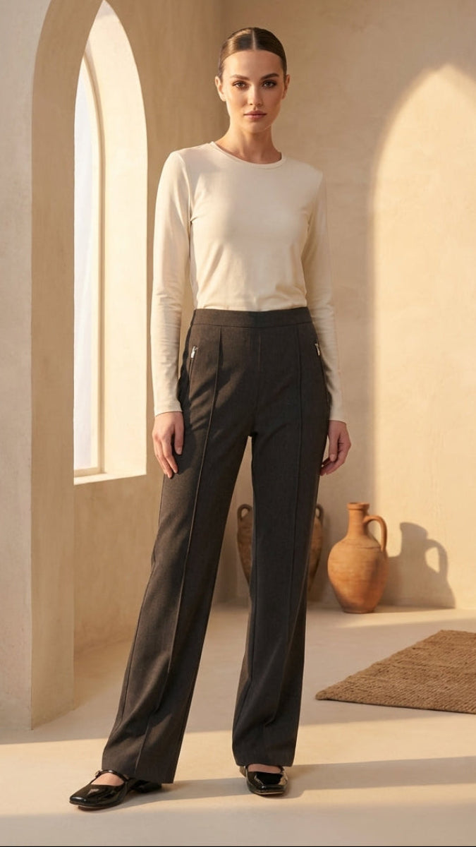 Woman wearing a white top and dark pants in a sunlit room with arches and a vase.