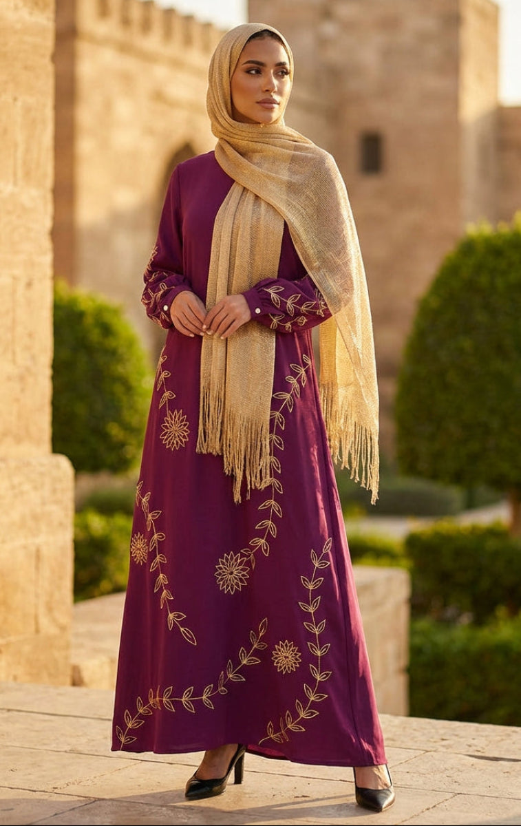 Woman in a purple dress with gold embroidery and beige hijab standing in front of a stone building.